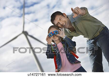 Stock Image - Girl (5-6) using binoculars with father at wind farm. Fotosearch