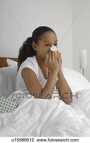 Stock Image - Girl (7-9) blowing nose in bed. Fotosearch