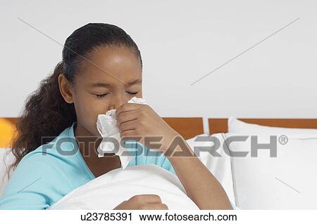 Stock Image - Girl (7-9) blowing nose in bed. Fotosearch