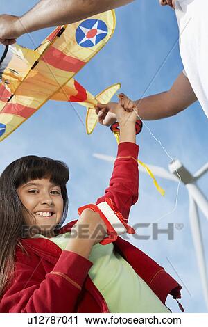 Girl (7-9) holding airplane kite with father at wind farm View Large Photo Image Stock Image - Girl (7-9) holding airplane kite with father at wind farm. Fotosearch
