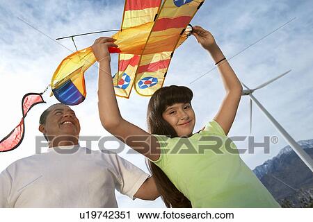 Stock Image - Girl (7-9) holding airplane kite with father at wind farm. Fotosearch