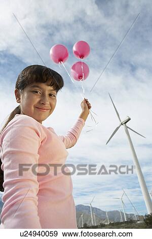 Stock Photo - Girl (7-9) holding balloons at wind farm, portrait. Fotosearch