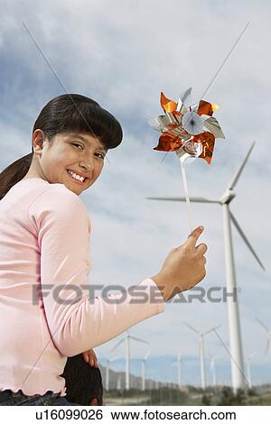 Stock Photograph - Girl (7-9) holding windmill, sitting on fathers shoulders at wind farm, portrait. Fotosearch