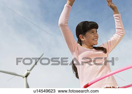 Stock Image - Girl (7-9) playing with hula hoop at wind farm. Fotosearch