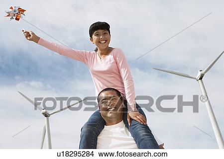 Picture - Girl (7-9) sitting on fathers shoulders at wind farm, portrait. Fotosearch