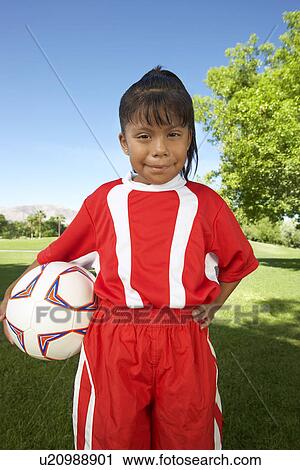Stock Image - Girl (7-9 years) soccer player holding ball under arm, portrait. Fotosearch