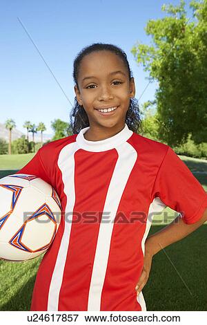 Stock Photo - Girl (7-9 years) soccer player holding ball under arm, portrait. Fotosearch