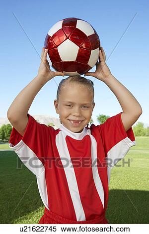 Stock Photography - Girl (7-9 years) soccer player holding ball above head, portrait. Fotosearch