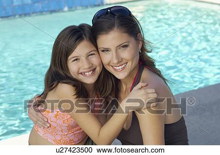 Stock Image - Girl embracing mother by swimming pool, portrait. Fotosearch