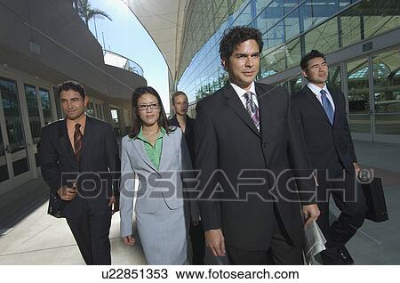 Stock Image - Group of business people walking past office building. Fotosearch