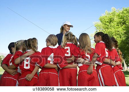 Stock Photo - Group of children soccer players embracing standing in front of coach, back view. Fotosearch