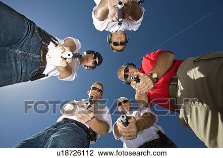 Stock Image - Group of people aiming guns in circle, low angle view. Fotosearch