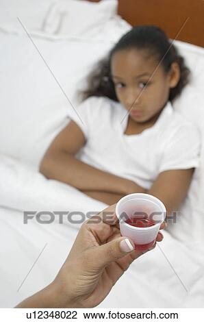 Stock Image - Hand holding medication for girl (7-9) lying in bed. Fotosearch