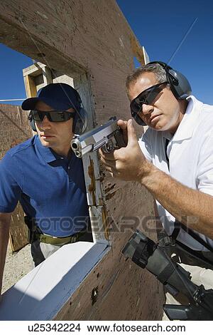 Instructor assisting man aiming hand gun at firing range View Large Photo Image Picture - Instructor assisting man aiming hand gun at firing range. Fotosearch