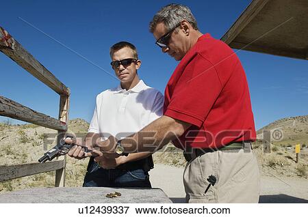 Stock Photo - Instructor assisting man loading hand gun at firing range. Fotosearch