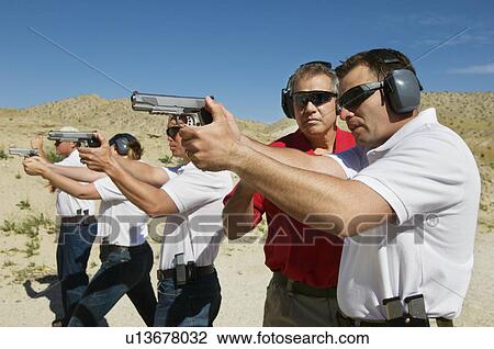 Instructor assisting men aiming hand guns at firing range View Large Photo Image Stock Image - Instructor assisting men aiming hand guns at firing range. Fotosearch