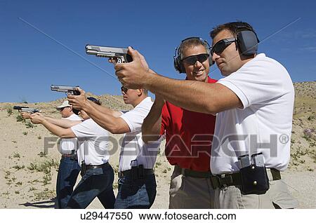 Instructor assisting men aiming hand guns at firing range View Large Photo Image Stock Image - Instructor assisting men aiming hand guns at firing range. Fotosearch