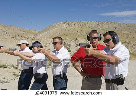 Stock Photograph - Instructor assisting men aiming hand guns at firing range. Fotosearch