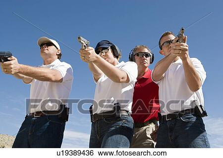 Instructor assisting people aiming guns at firing range View Large Photo Image Stock Photograph - Instructor assisting people aiming guns at firing range. Fotosearch