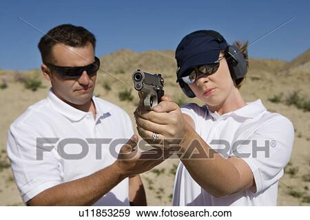 Stock Photo - Instructor assisting woman aiming hand gun at firing range in desert. Fotosearch