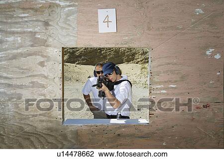 Stock Image - Instructor assisting woman aiming machine gun at firing range. Fotosearch