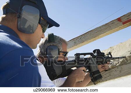 Stock Photo - Instructor with man aiming machine gun at firing range. Fotosearch