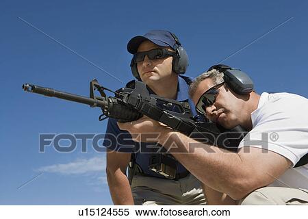 Stock Photography - Instructor with man aiming machine gun at firing range, low angle view. Fotosearch