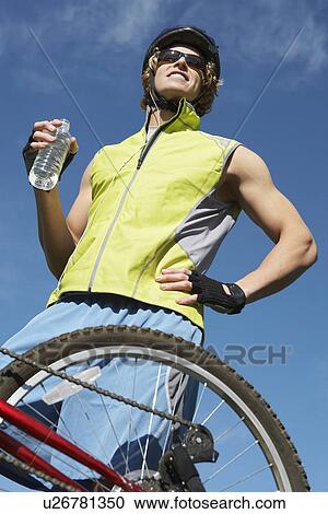 Stock Image - Male cyclist holding water bottle, outdoors. Fotosearch