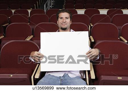 Stock Photo - Male student holding blank board in lecture theatre, portrait. Fotosearch