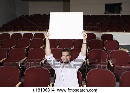 Male student holding blank board over head, in lecture theatre, portrait View Large Photo Image Picture - Male student holding blank board over head, in lecture theatre, portrait. Fotosearch