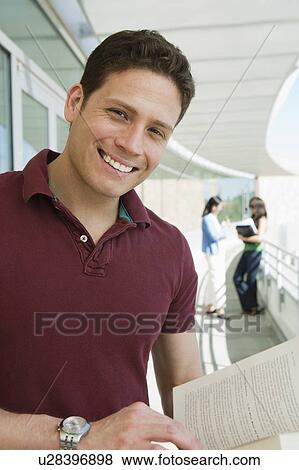 Stock Photo - Male student holding book at school, smiling, portrait. Fotosearch