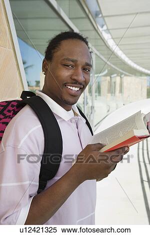 Stock Photography - Male student holding book at school, smiling, portrait. Fotosearch