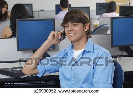 Stock Image - Male student using mobile phone in computer classroom. Fotosearch