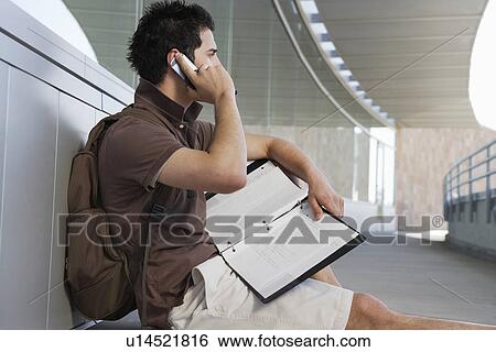 Stock Photograph - Male student using mobile phone outside school. Fotosearch