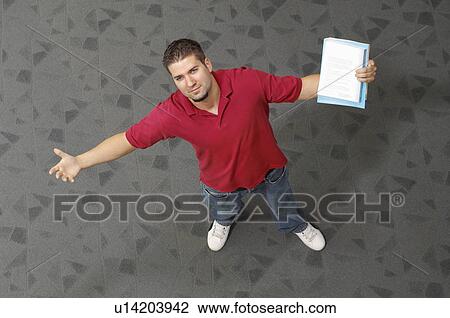 Stock Image - Male student with arms outstretched, indoors, portrait. Fotosearch