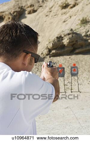 Stock Image - Man aiming hand gun at firing range. Fotosearch