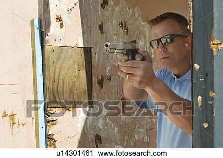 Stock Image - Man aiming hand gun at firing range. Fotosearch