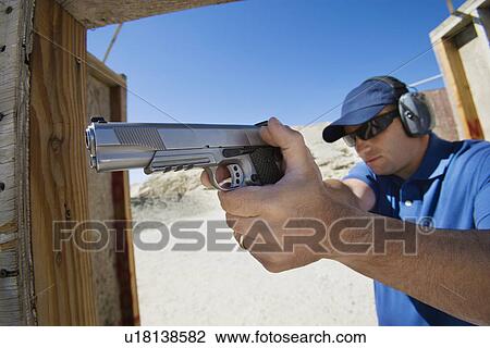 Stock Image - Man aiming hand gun at firing range. Fotosearch