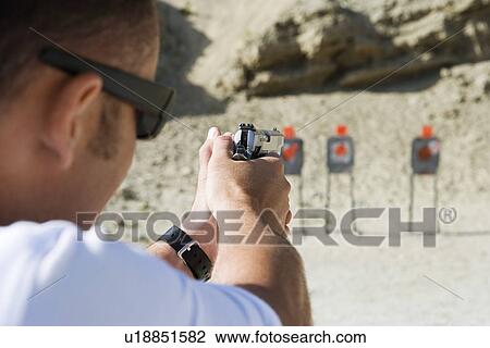 Stock Image - Man aiming hand gun at firing range. Fotosearch