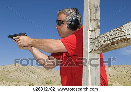 Stock Image - Man aiming hand gun at firing range. Fotosearch