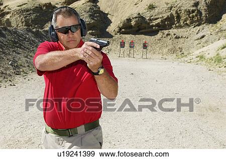 Stock Photo - Man aiming hand gun at firing range. Fotosearch