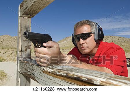 Stock Photo - Man aiming hand gun at firing range. Fotosearch