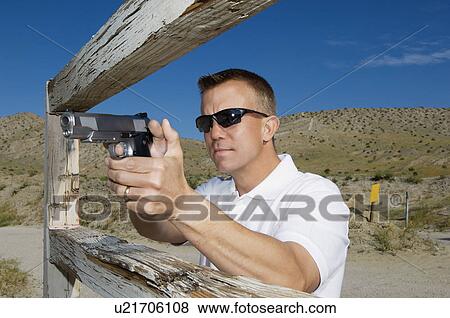 Stock Photo - Man aiming hand gun at firing range. Fotosearch
