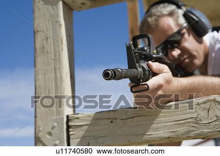 Stock Image - Man aiming machine gun at firing range. Fotosearch