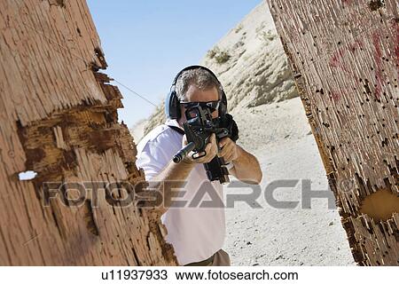 Stock Image - Man aiming machine gun at firing range. Fotosearch