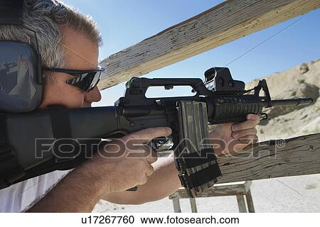 Stock Image - Man aiming machine gun at firing range. Fotosearch