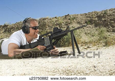 Stock Image - Man aiming machine gun at firing range. Fotosearch