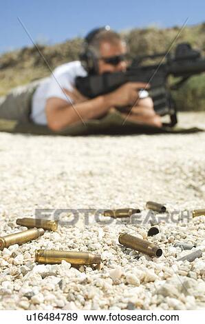 Stock Photo - Man aiming machine gun at firing range, focus on bullets in foreground. Fotosearch