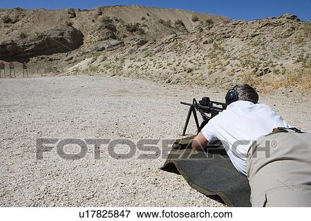 Stock Photo - Man aiming machine gun at firing range. Fotosearch