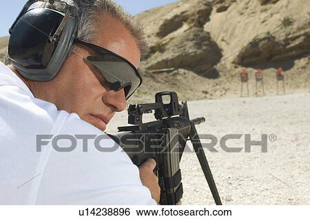 Stock Photograph - Man aiming machine gun at firing range. Fotosearch